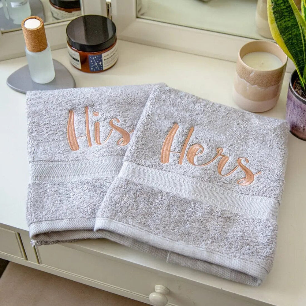 silver towels with His and Hers embroidered, shown on a bedroom vanity table