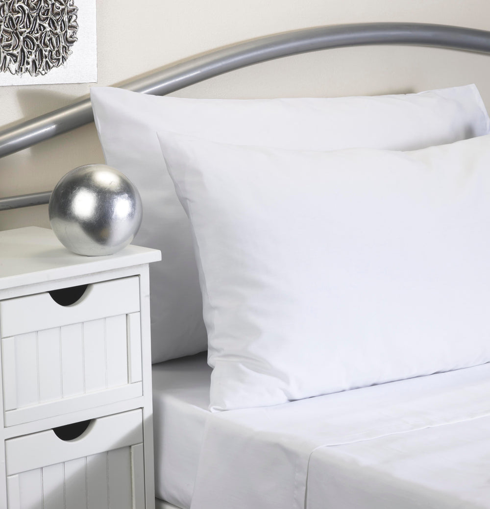 White cotton pillowcases and matching white bed sheets displayed on a bed with a metallic silver headboard, next to a white wooden nightstand with a silver decorative sphere.