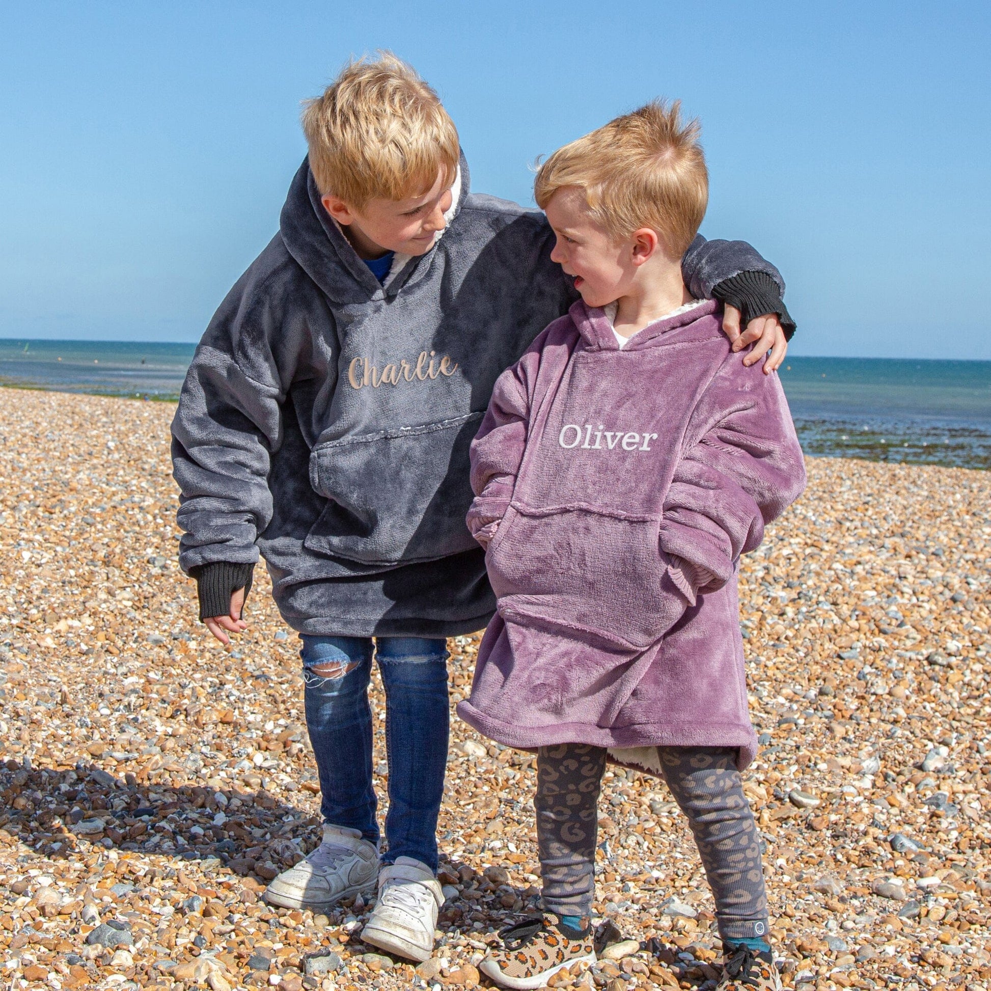 Two kids standing on a beach wearing Hooded Wearable Blanket