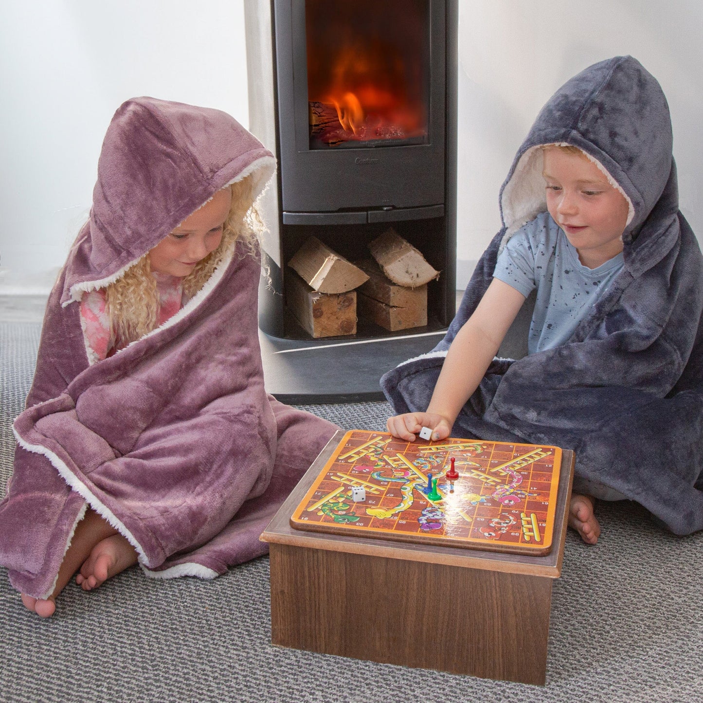 Two Kids wearing Hooded Sherpa Blanket next to a fireplace