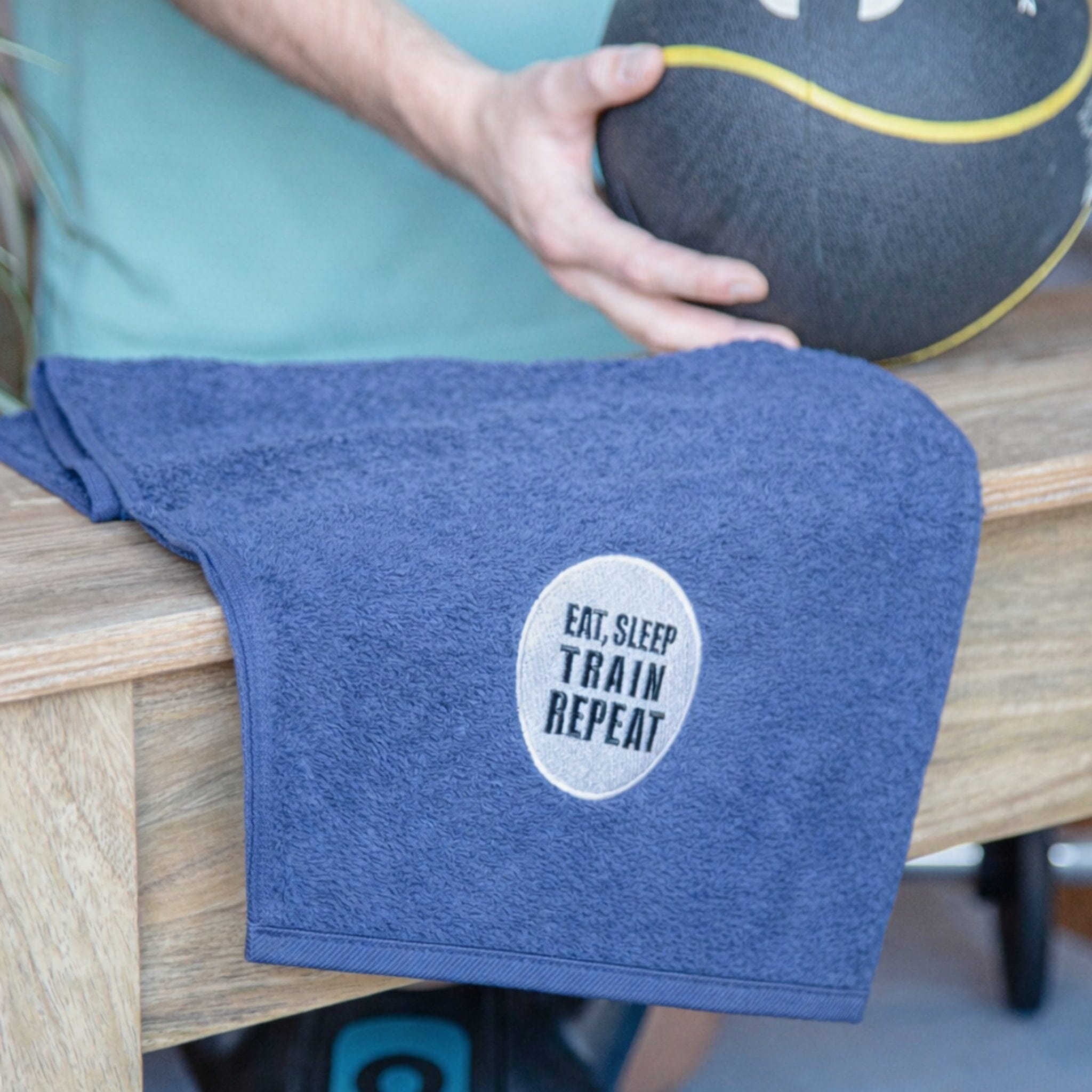 Blue towel with 'Eat, Sleep, Train, Repeat' text on a wooden surface.