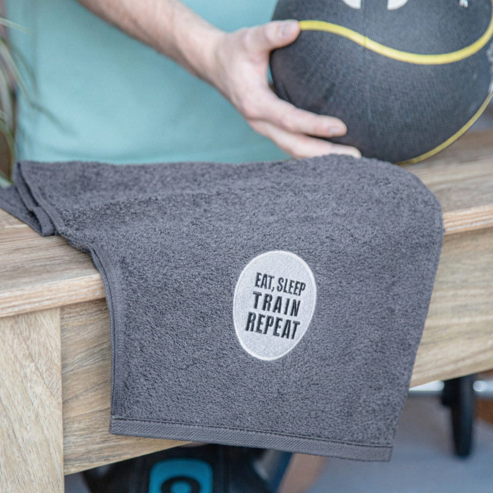 Gray towel with 'Eat. Sleep. Train. Repeat.' text on a wooden surface.