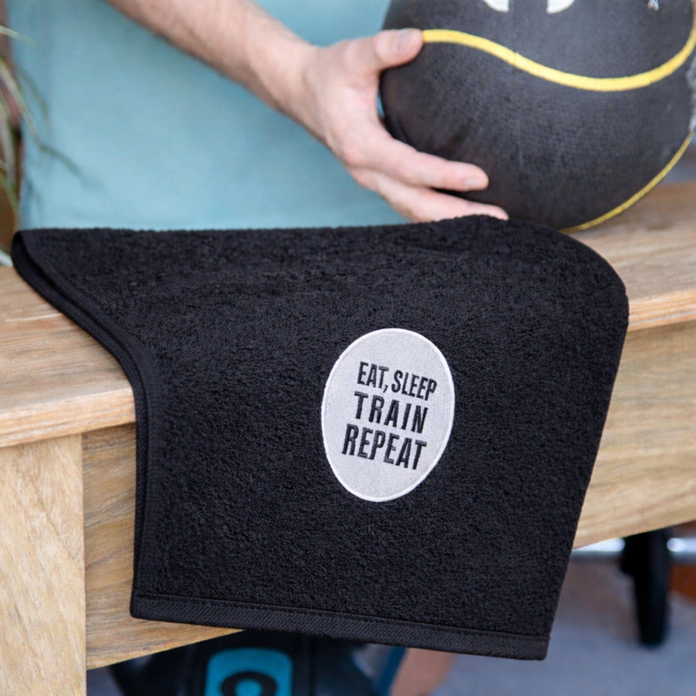Black towel with 'Eat. Sleep. Train. Repeat.' text on a wooden surface.