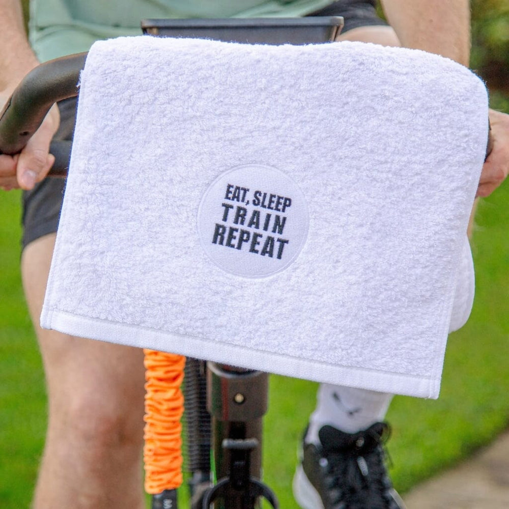 White towel with 'EAT, SLEEP TRAIN REPEAT' text held by a person on a bike.