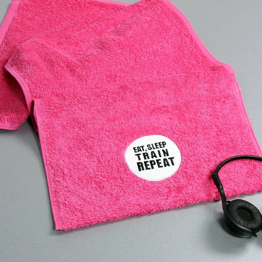 Pink towel with 'Eat. Sleep. Train. Repeat.' sticker on a gray background