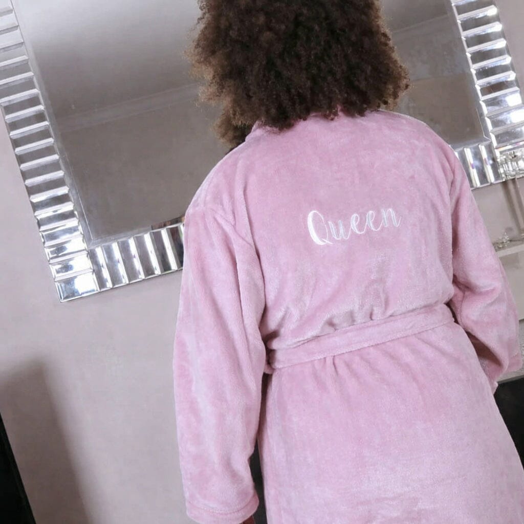 Person wearing a pink robe with 'Queen' embroidered on the back, standing in front of a mirror.