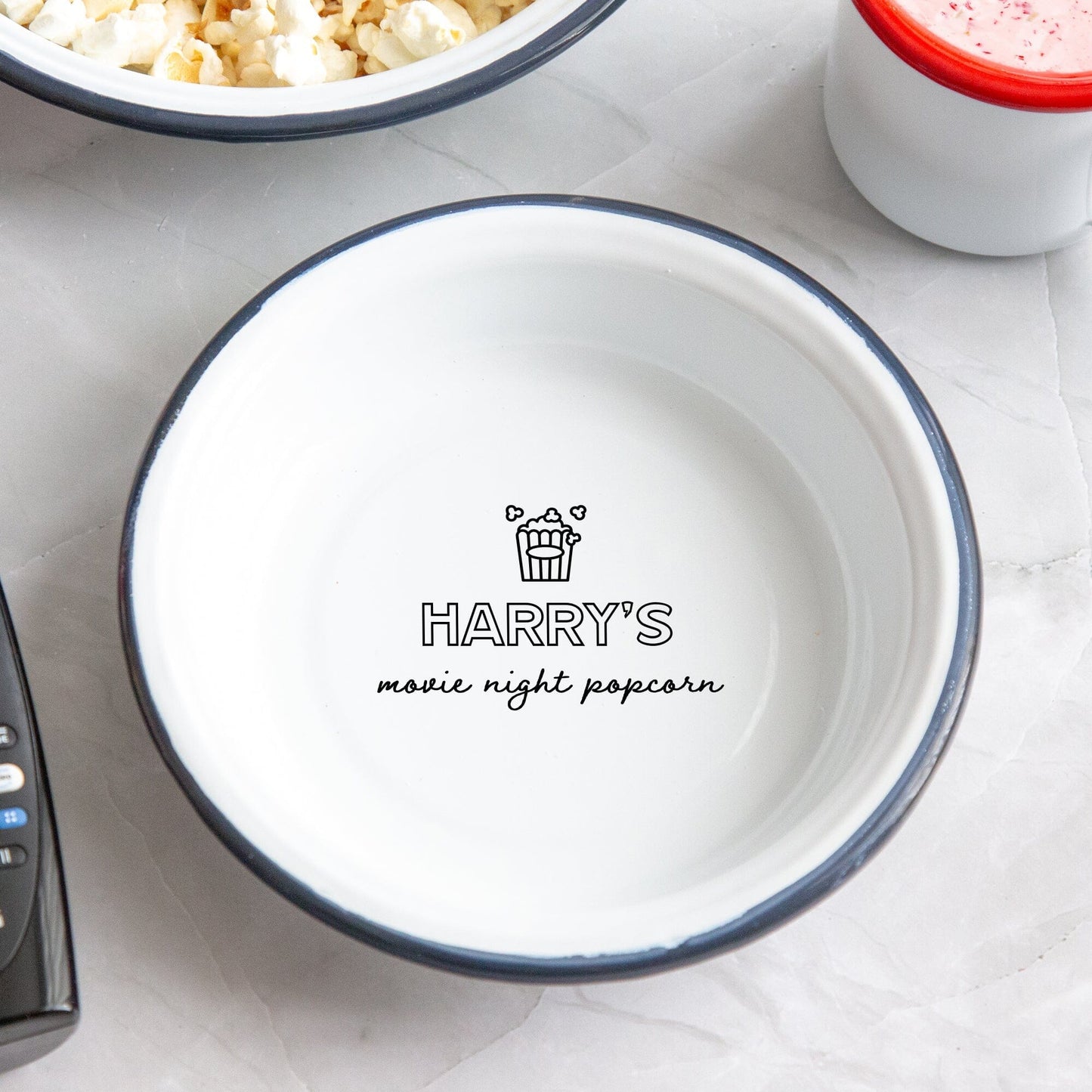 Personalised Children's Popcorn Enamel Bowl on the table. A remote popcorns and hot chocolate around