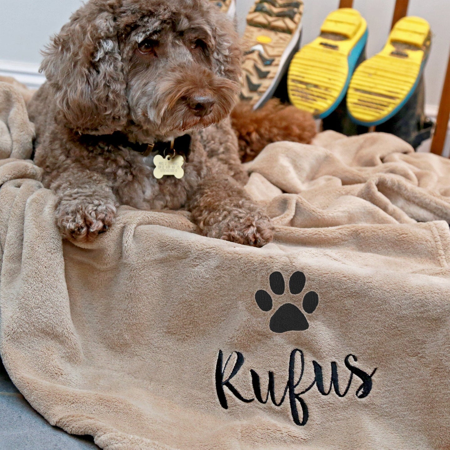 Stone coloured dog blanket with Rufus embroidered underneath a paw print. Rufus is enjoying the blanket.