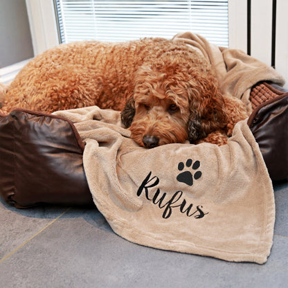 Stone coloured dog blanket with Rufus embroidered underneath a paw print. Rufus is enjoying the blanket.