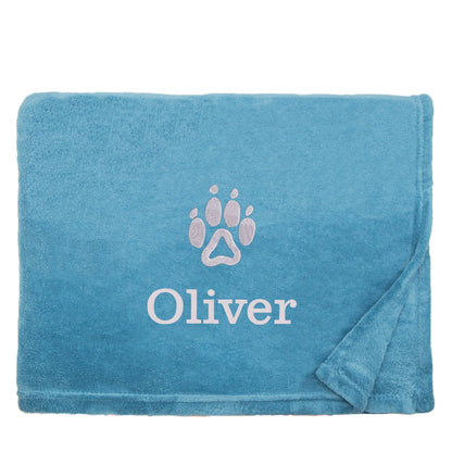A peacock blue dog blanket with Oliver's name on it, underneath a paw print design