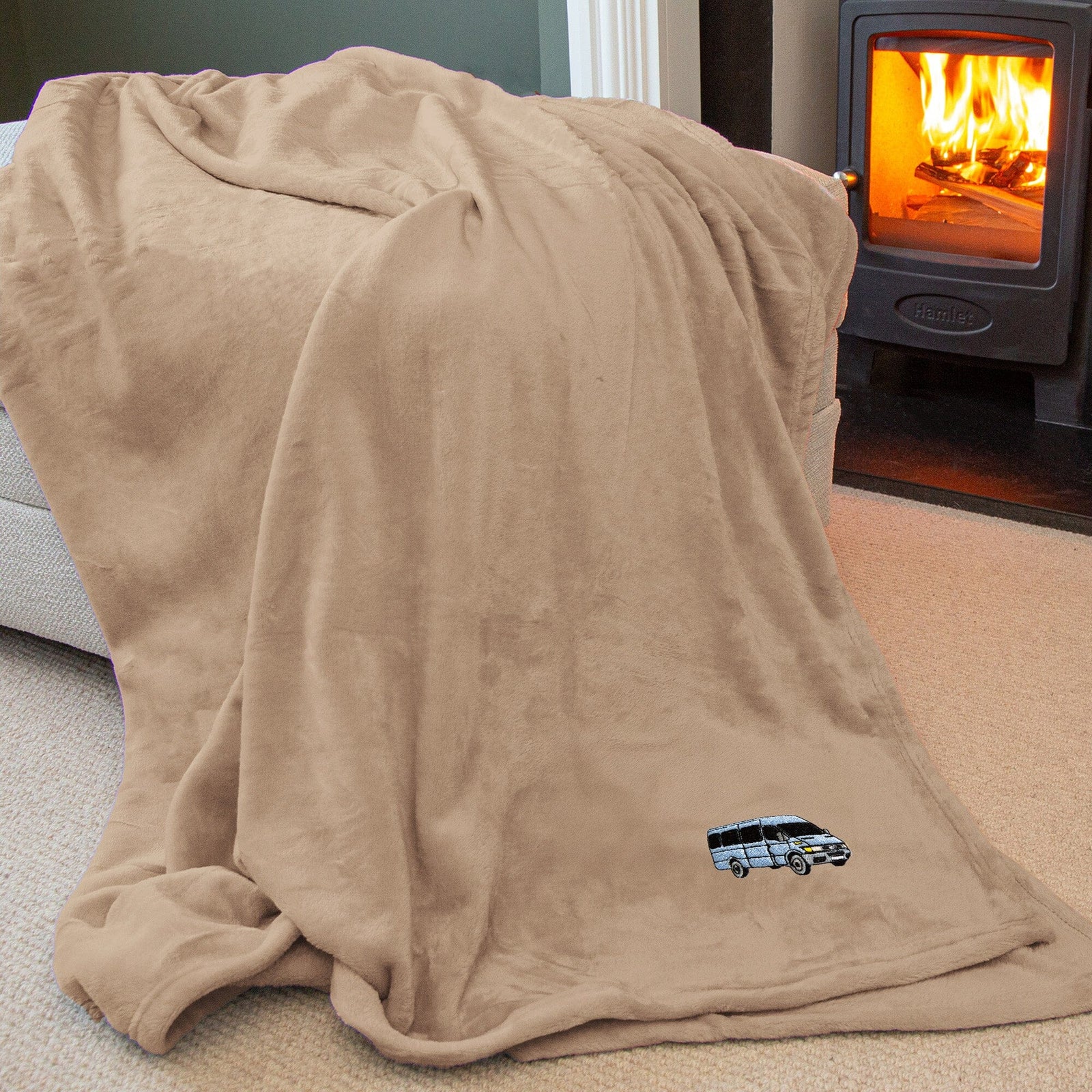 A beige fleece throw blanket draped over a chair in a living room setting, with a burning wood-burning stove visible in the background.