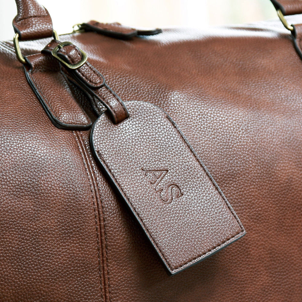 personalised faux leather holdall in brown with a debossed luggage tag