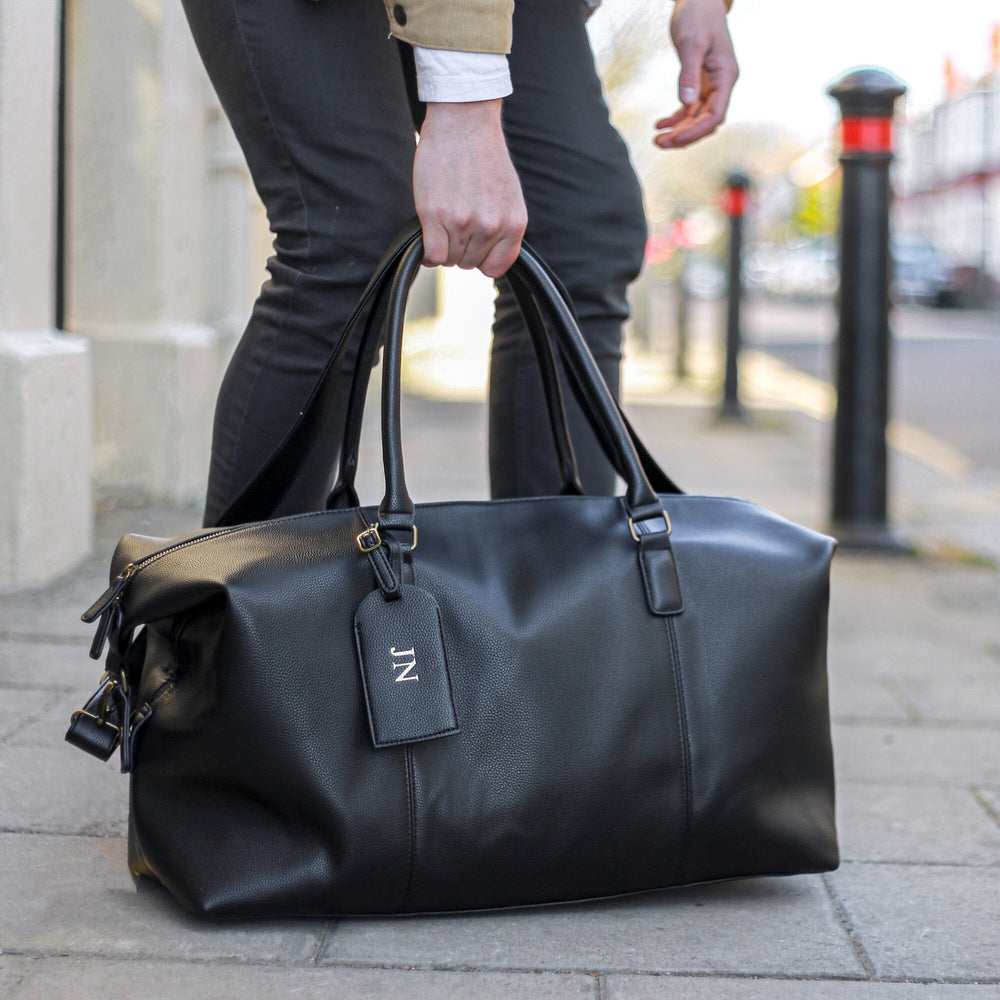 personalised faux leather holdall in black with a debossed luggage tag