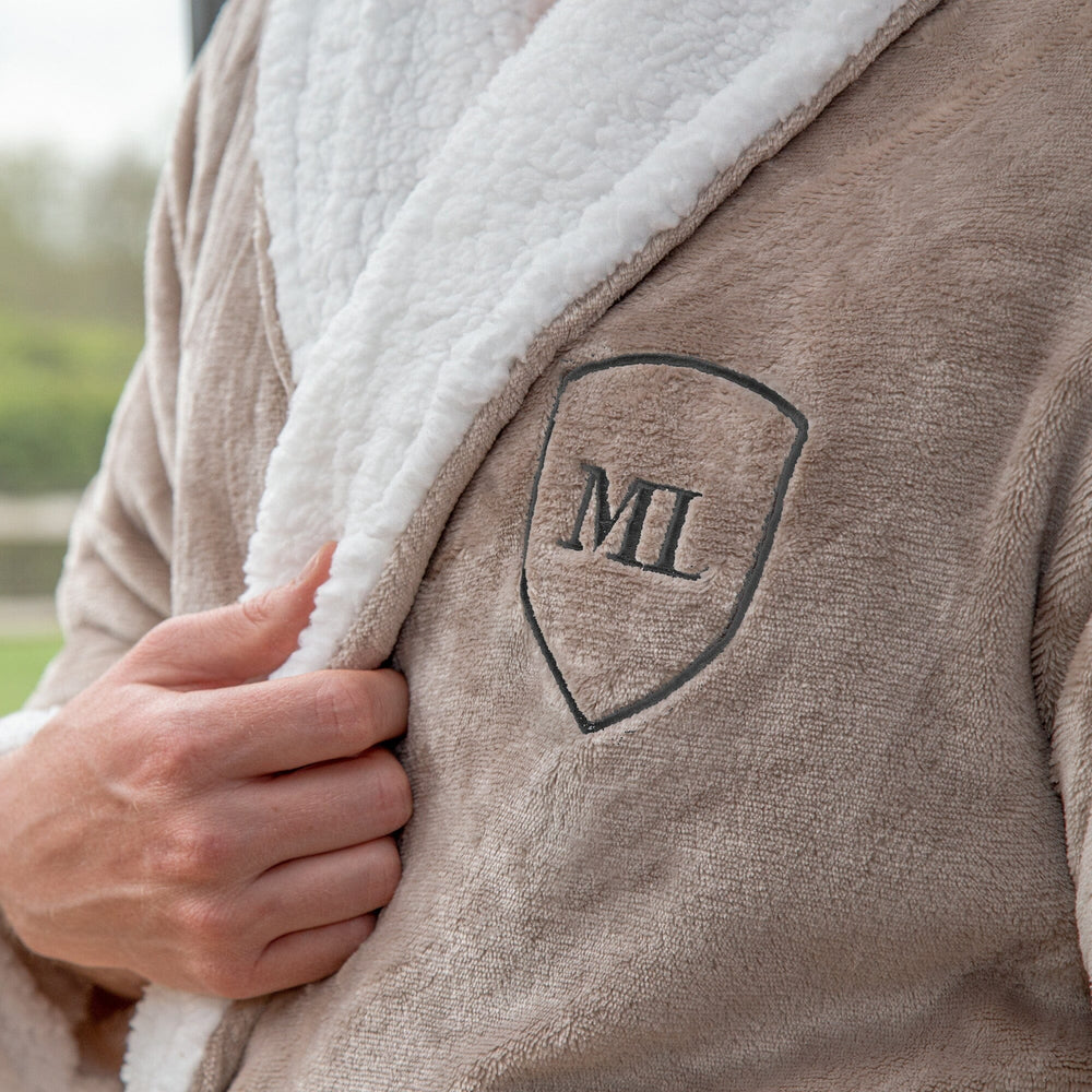 Close-up of a monogrammed sherpa robe with white sherpa lining and embroidered initials 'ML' on a blurred outdoor background