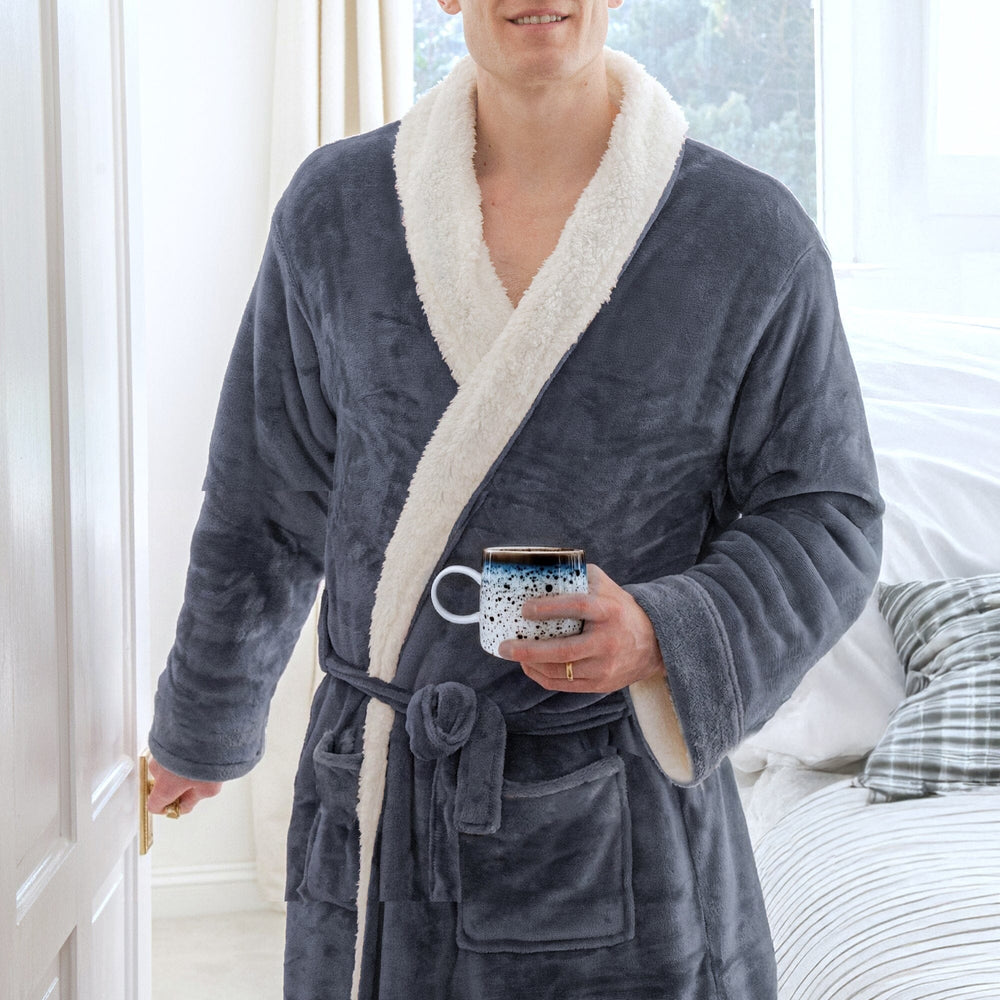 Person wearing a slate sherpa robe with white trim, holding a mug in a bedroom setting.