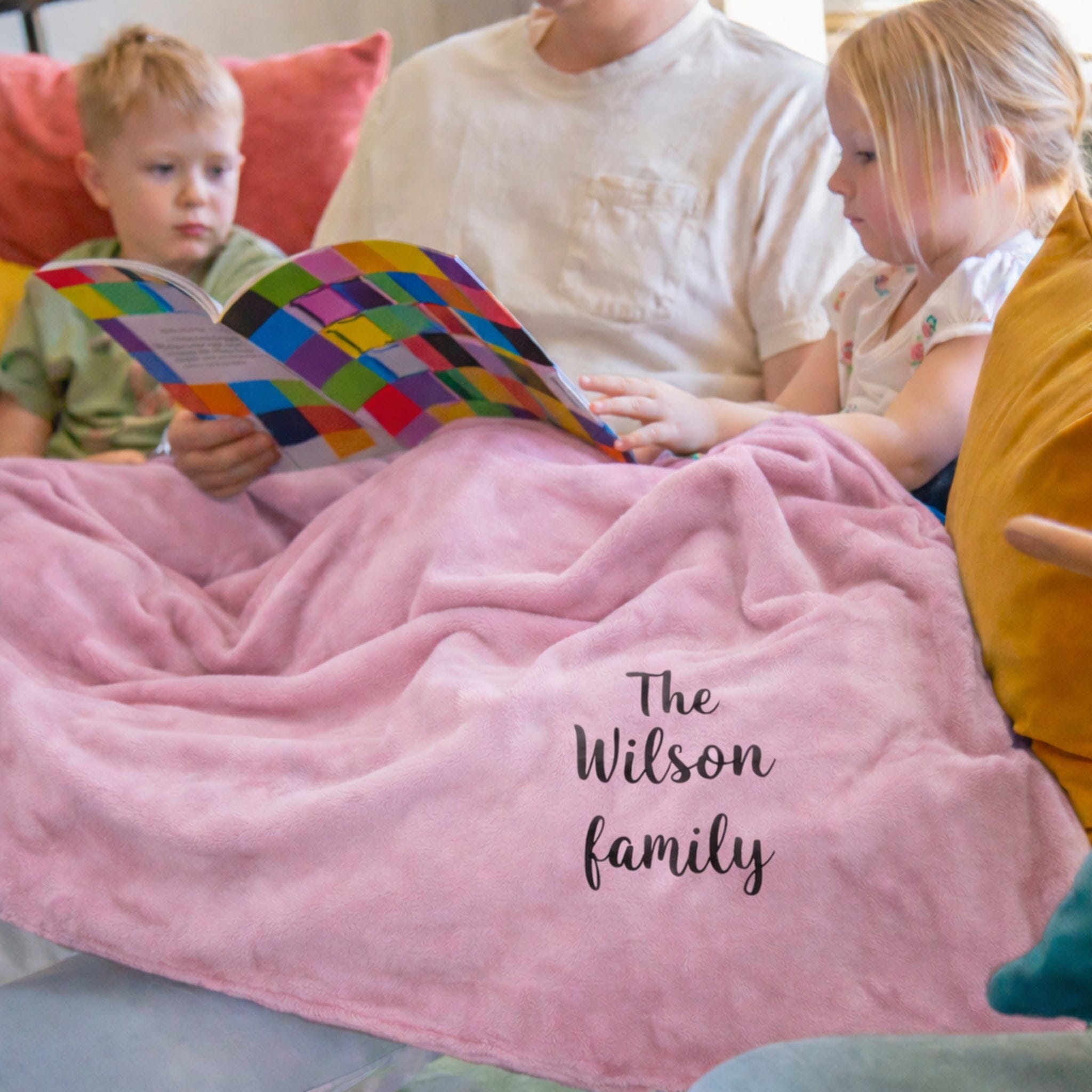 Family reading a book together on a couch with a pink blanket, personalized with 'The Wilson family'.