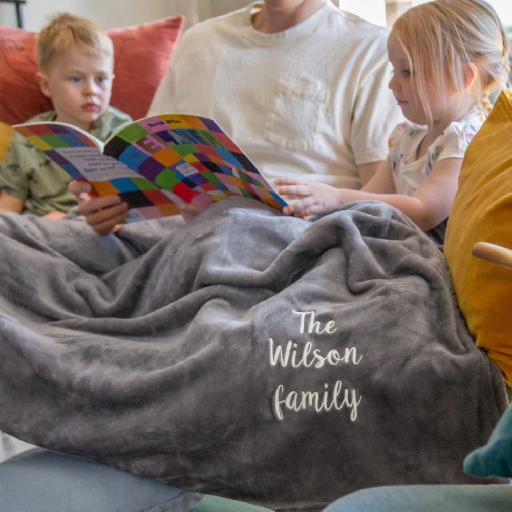 Family reading a book together under a personalized gray blanket