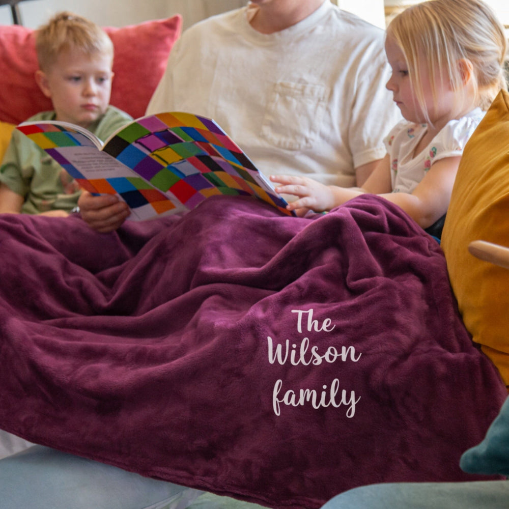Family sitting on a couch with a colorful book, covered by a purple blanket with 'The Wilson family' text.