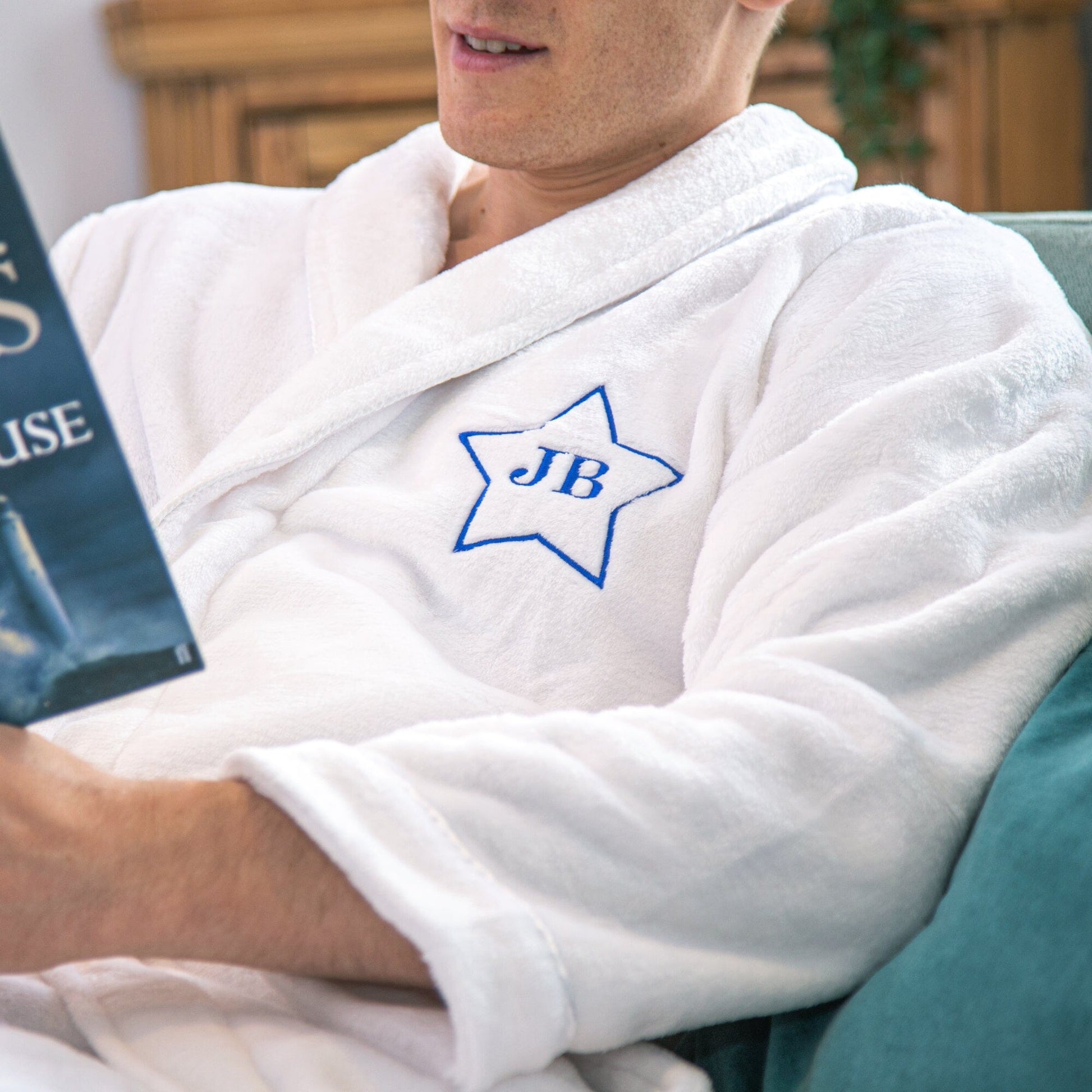 A male model sitting on a couch wearing a Personalised Super Soft Star Monogrammed Robe in White