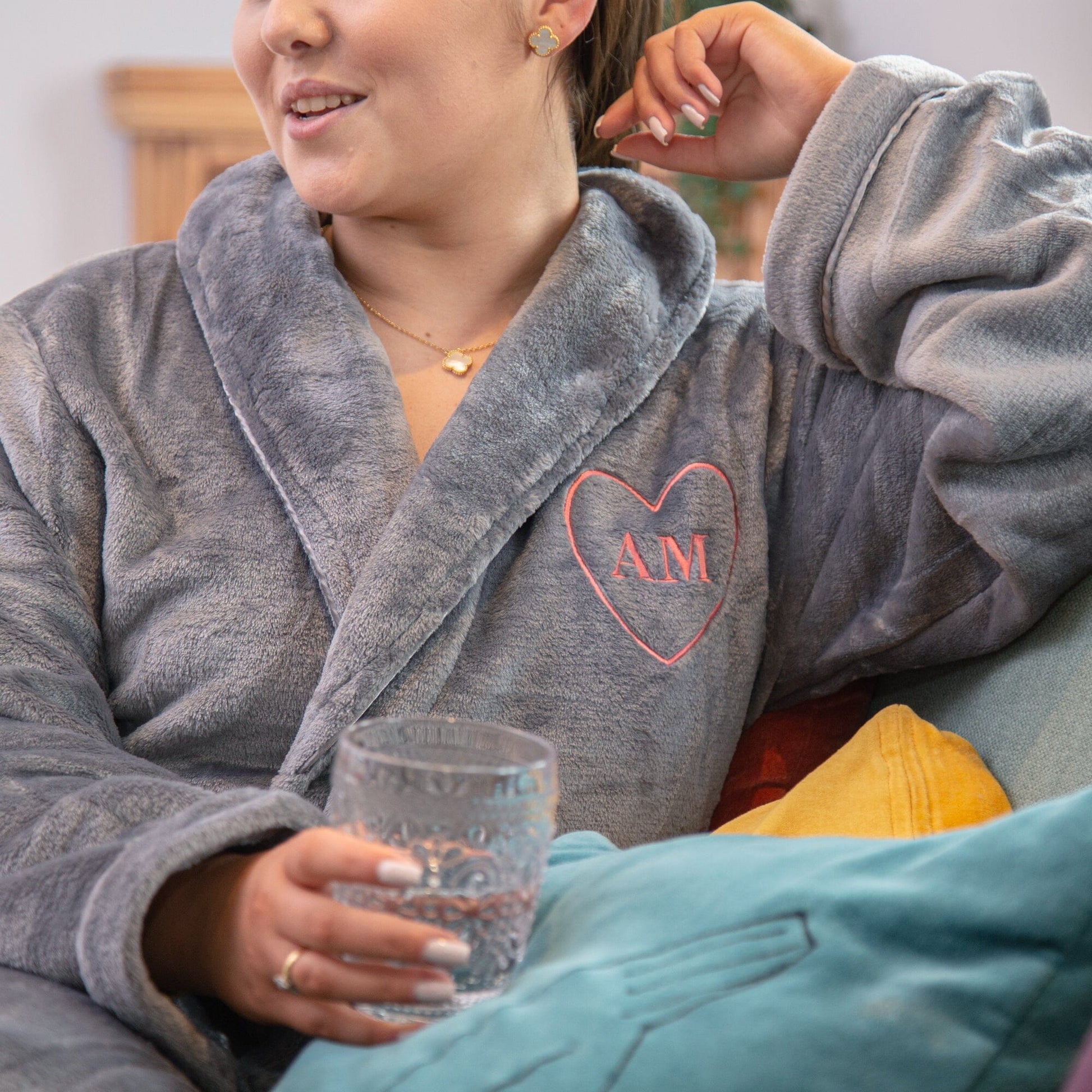 A female model sitting on a couch wearing a Personalised Super Soft Heart Monogrammed Robe in slate