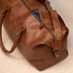 Brown leather duffel bag with 'DAD' strap on a beige surface