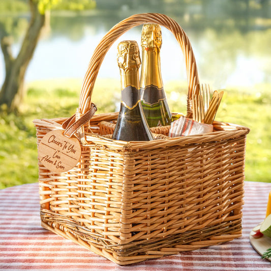A personalised wicker wine carrier basket is in a picnic outdoor spot. Featuring a personalised cherry wood veneer tag