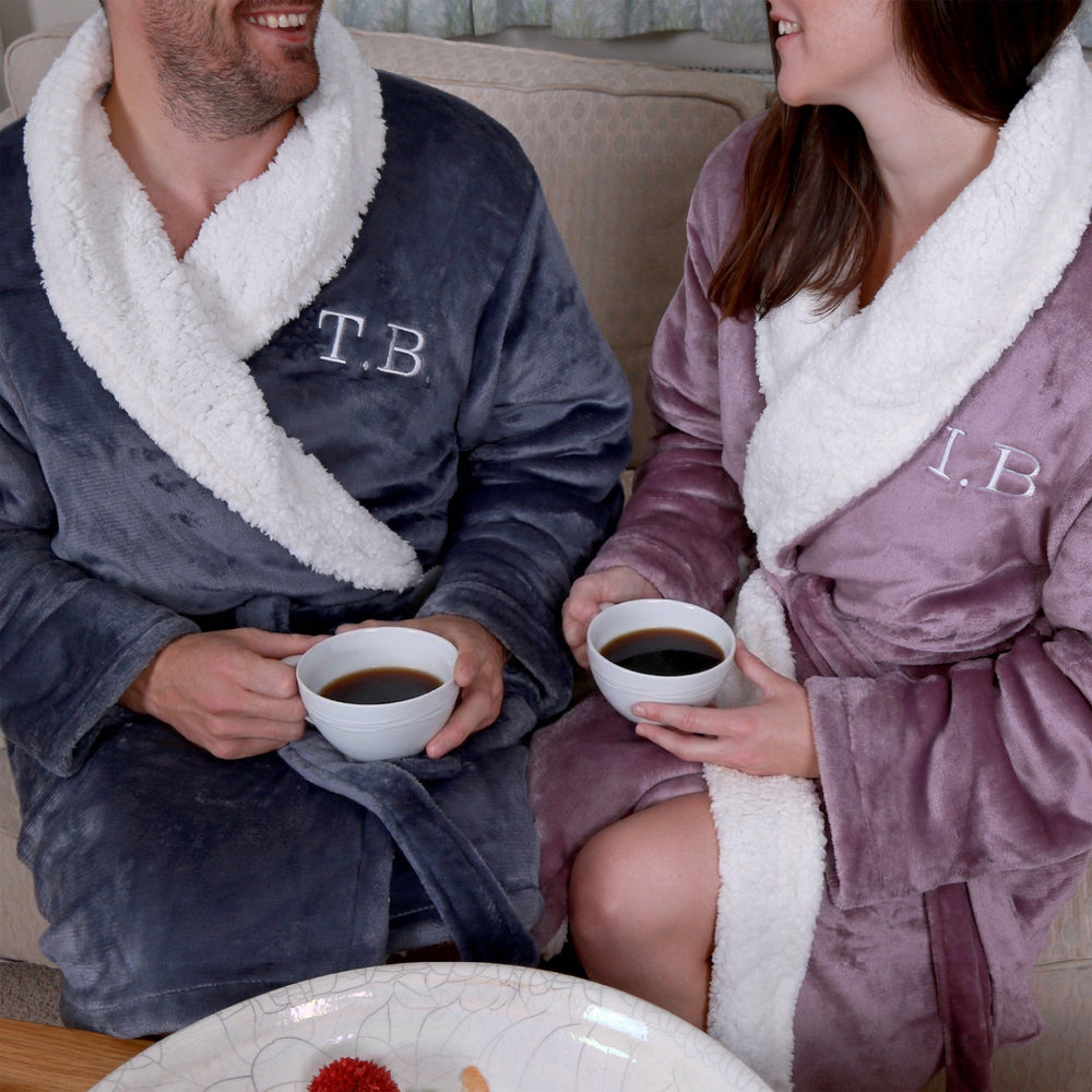 Two people in personalised sherpa robes with initials, sitting together holding coffee cups.