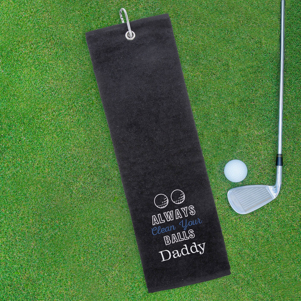 Black golf towel with humorous text on a green grass background