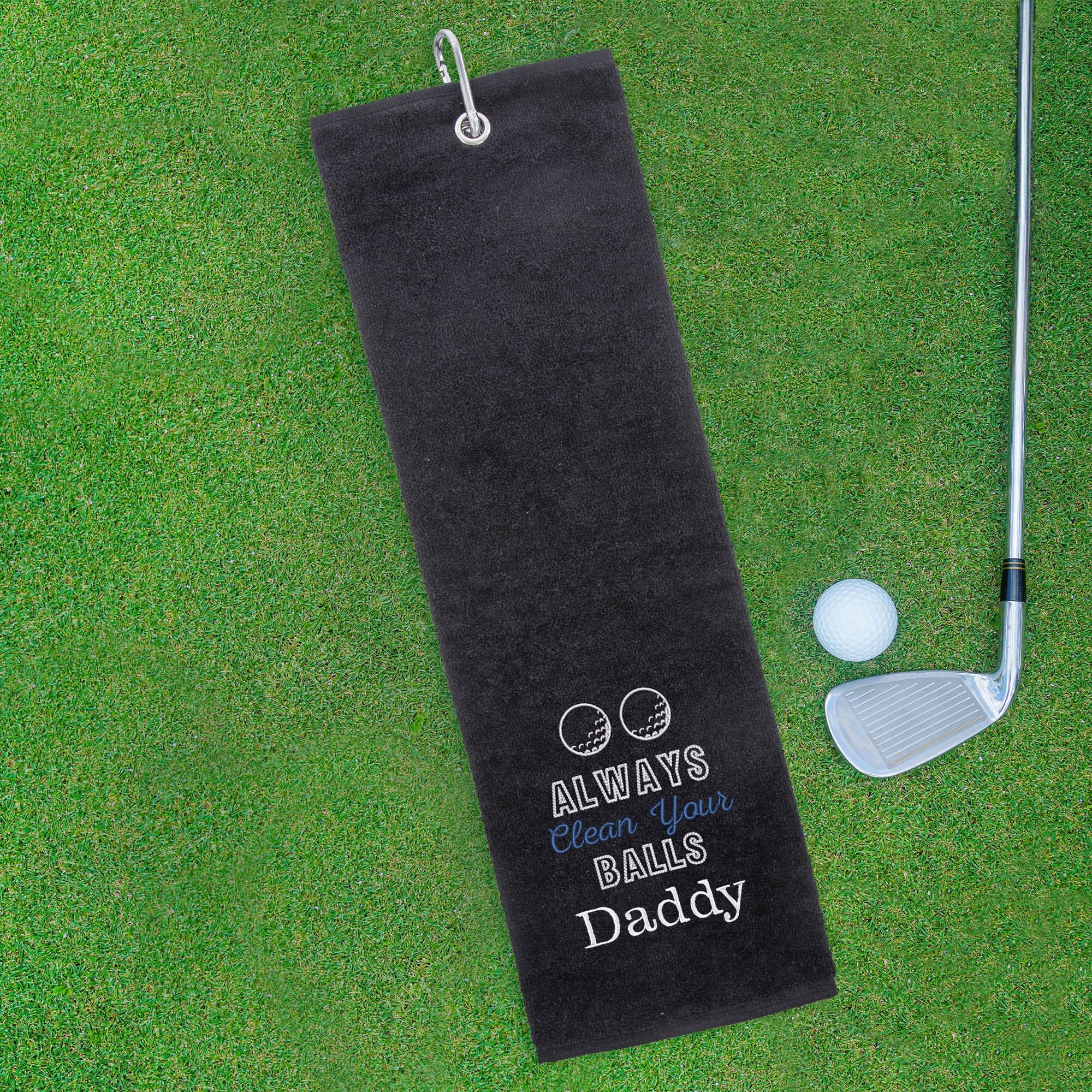 Black golf towel with humorous text on a green grass background