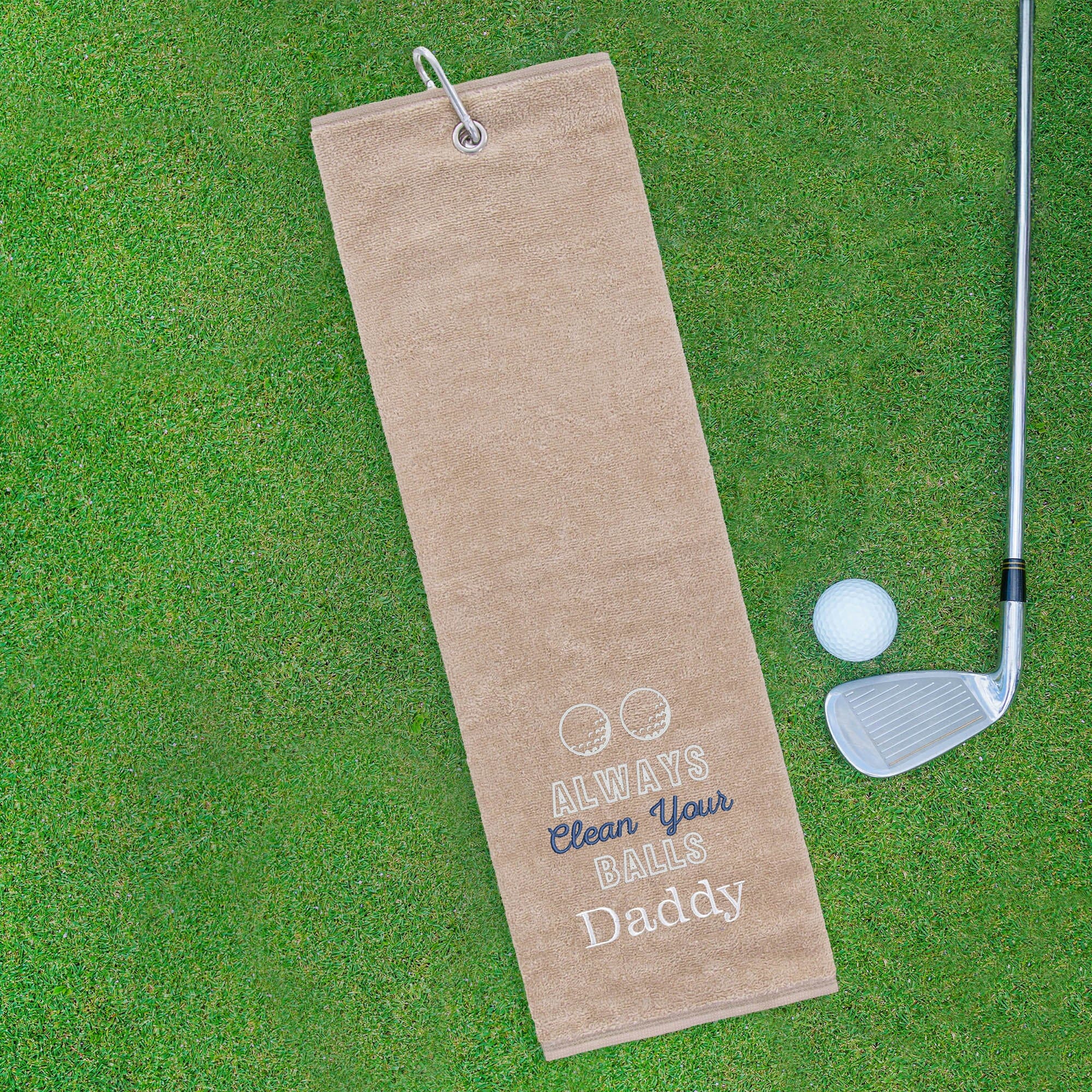 Beige golf towel with humorous text on a green grass background with golf club and ball.