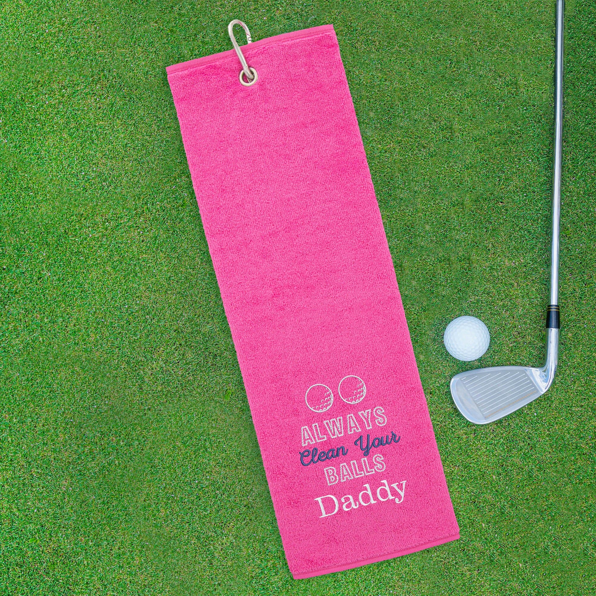 Pink golf towel with humorous text on a green golf course