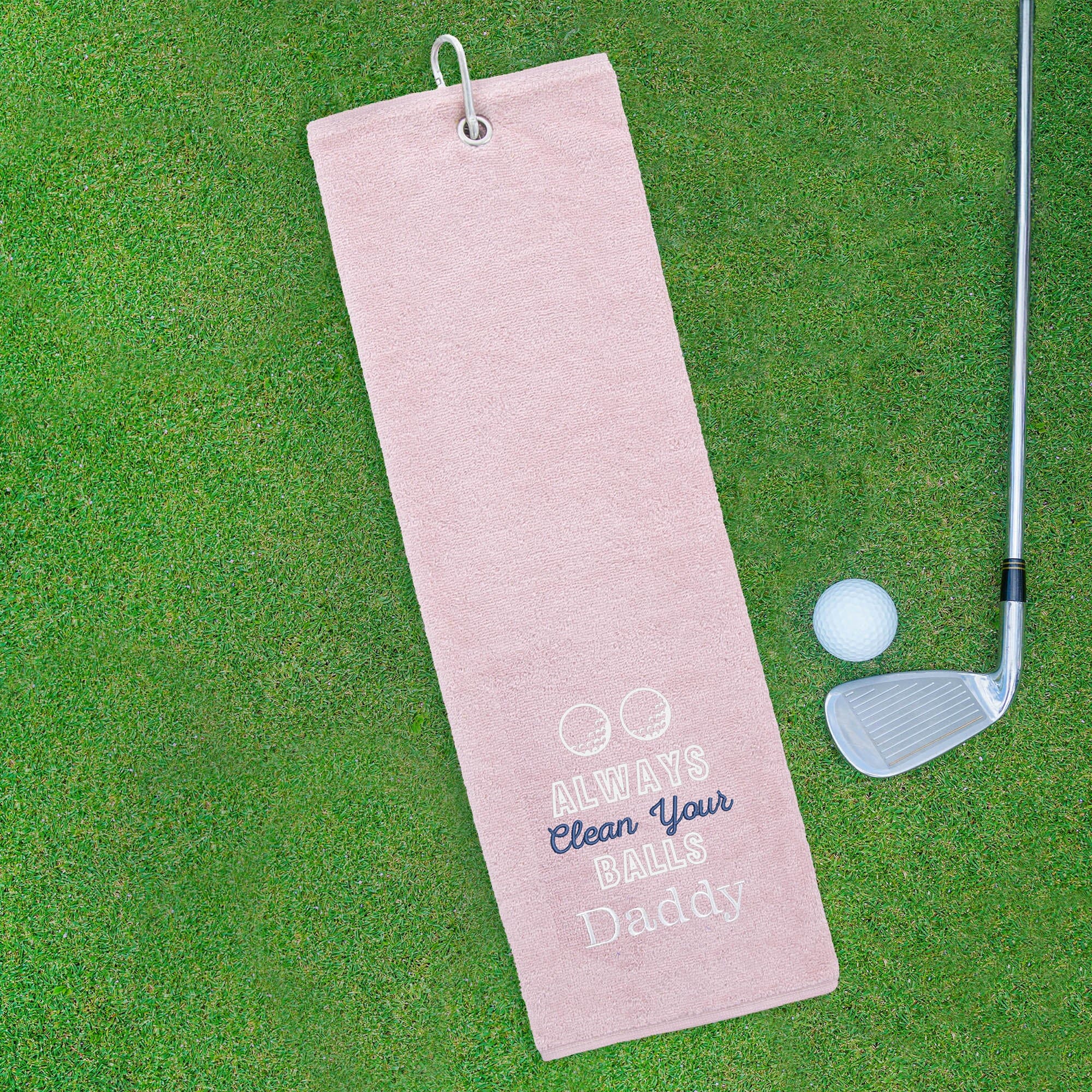 Pink golf towel with humorous text on a green golf course