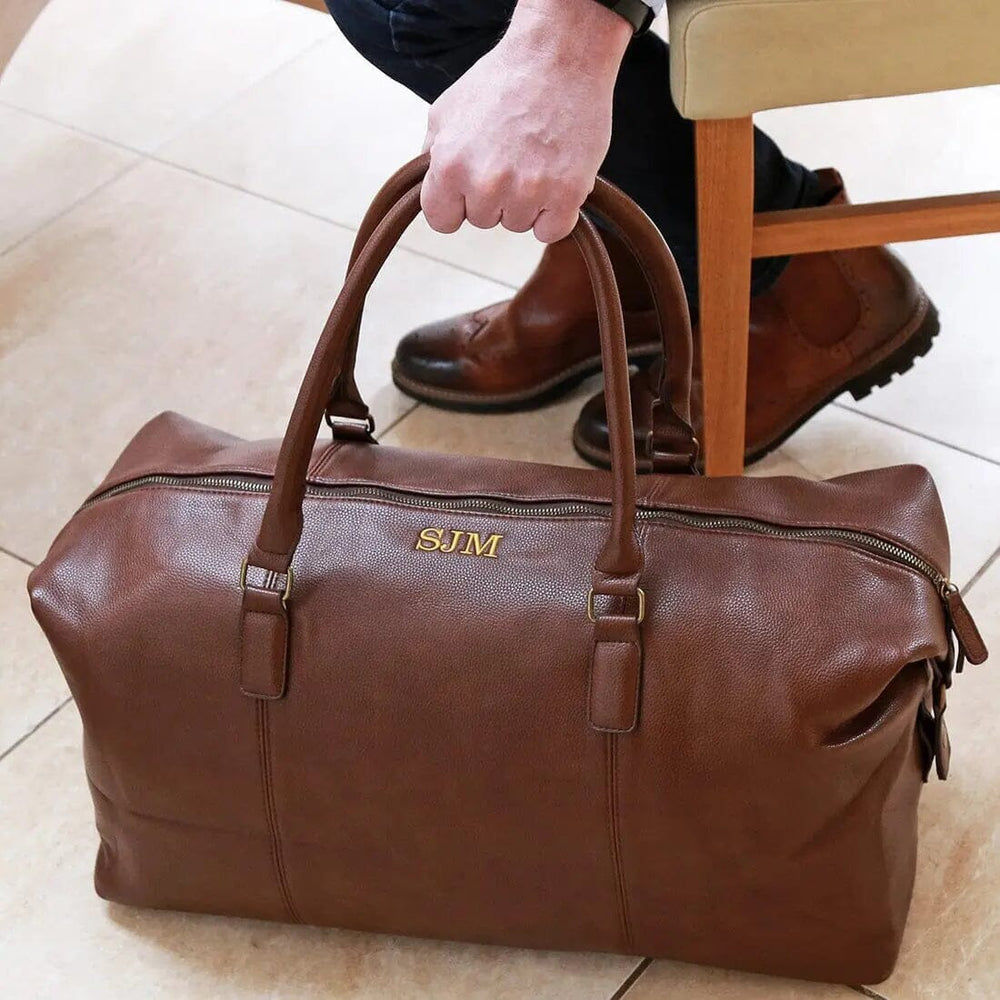 Personalised Vintage Holdall In Brown a male model picking it next to a stool