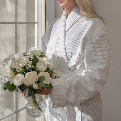 woman wearing a white waffle bathrobe gripping a vase of flowers