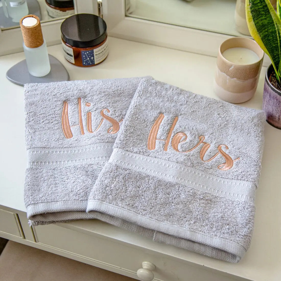 silver towels with His and Hers embroidered,  shown on a bedroom vanity table