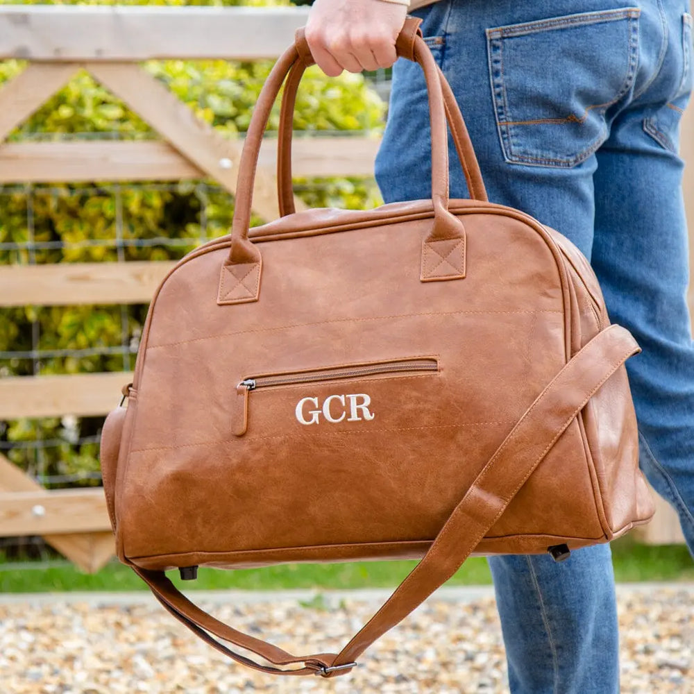 A Male model holding Faux Leather Overnight Bag In Brown   